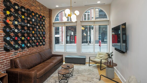 A cozy room with a brick wall, a leather sofa, a small table, and a large window with arched tops. - The Record Room -steps to Broadway & Printer’s Alley (Nashville)