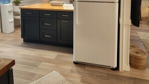 Une cuisine moderne avec un réfrigérateur blanc, des armoires noires et un plan de travail en bois.