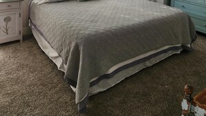 Une chambre à coucher comprenant un lit, deux tables de chevet, une commode, une fenêtre avec des stores, un ventilateur de plafond, un appareil de climatisation et un téléviseur.