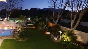 Un patio trasero con piscina, mobiliario exterior y una zona ajardinada bien iluminada.