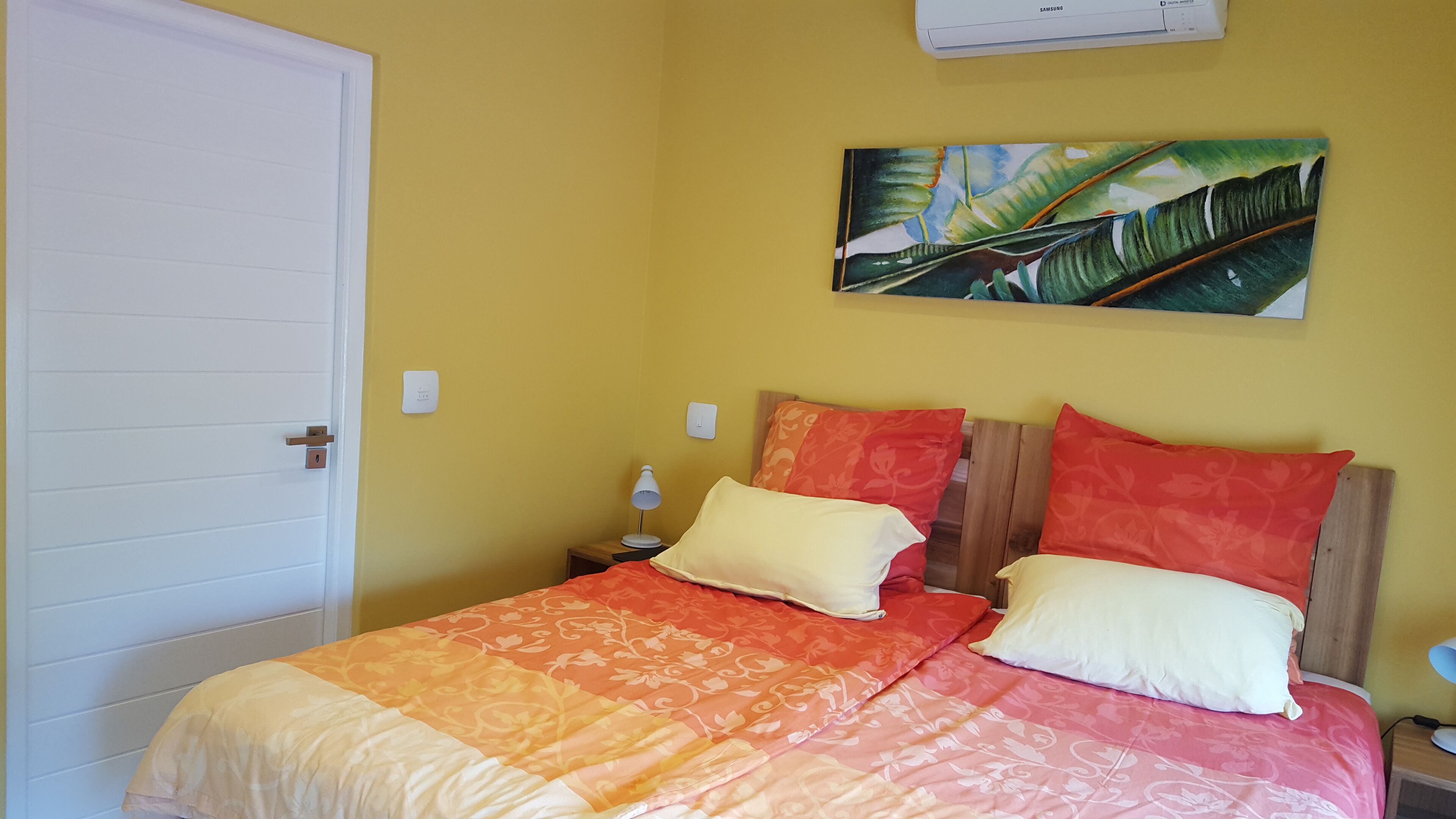 Une chambre à coucher comprenant un lit, deux lampes de chevet, une table de chevet, une porte et un climatiseur fixé au mur.