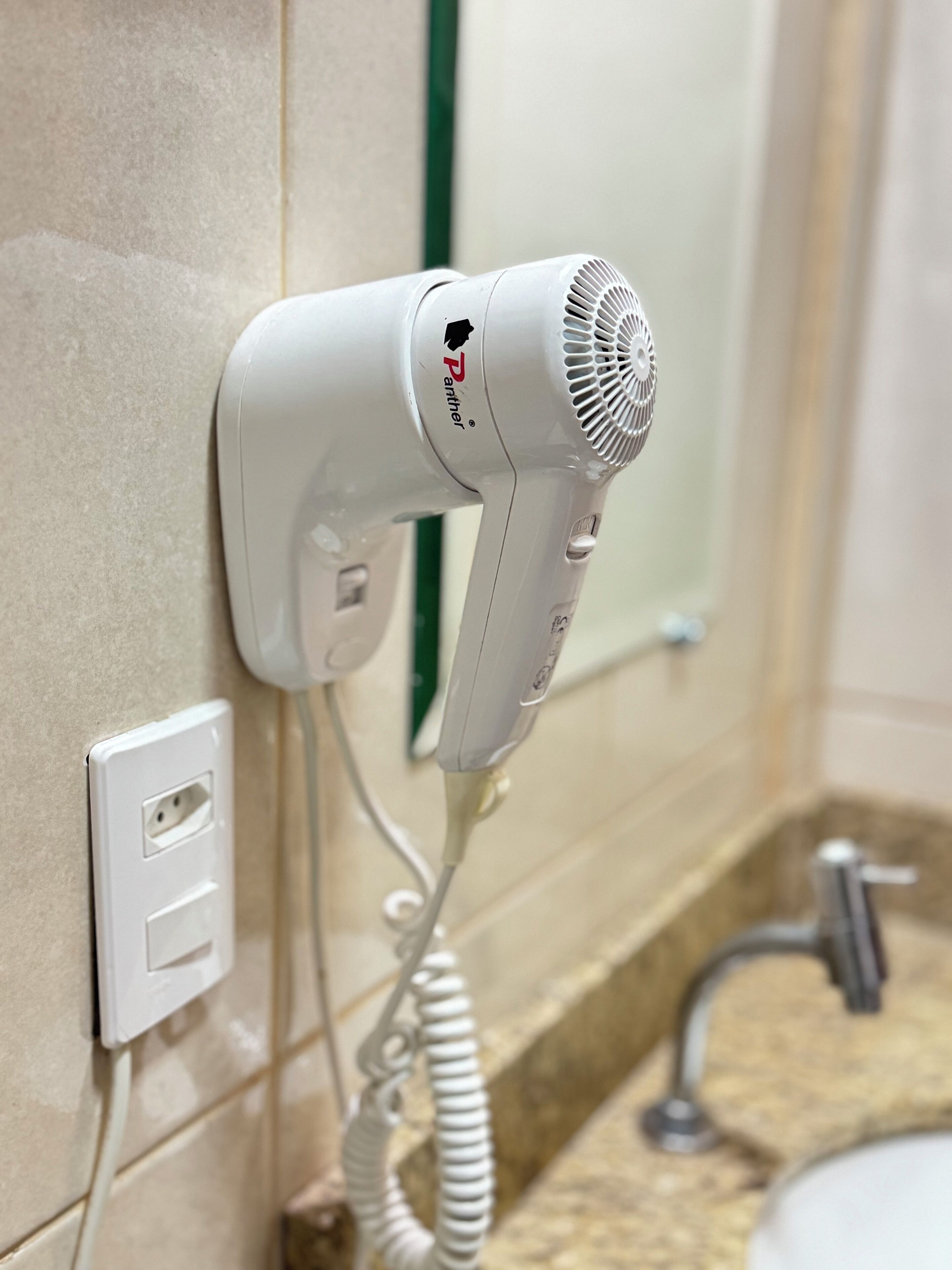 A hair dryer mounted on a wall in a bathroom with a tiled floor and a sink.