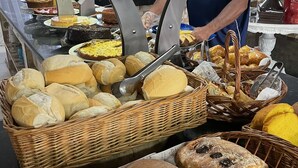 A buffet with various breads and pastries, a person serving, and a decorative vase. - Hotel Marazul (Cananeia)