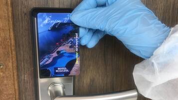 Une main portant un gant bleu insère une carte-clé d’hôtel dans la serrure d’une porte.
