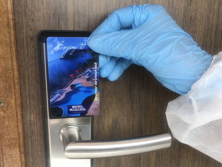 Une main portant un gant bleu insère une carte-clé d’hôtel dans la serrure d’une porte.