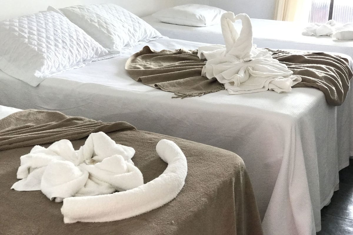 Two hotel beds with white linens, a brown blanket, and a white towel shaped like a swan.