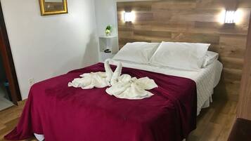 A neatly made bed with a red blanket, white pillows, and two white towels arranged on the bed.