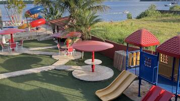 Ein Spielplatz mit Rutschen und Tischen, umgeben von Palmen und Blick auf das Wasser.