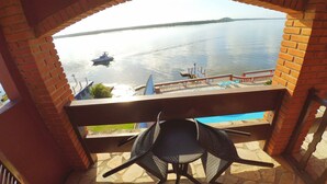 A balcony with a view of a calm lake, a boat, and a distant island. - Hotel Marazul (Cananeia)