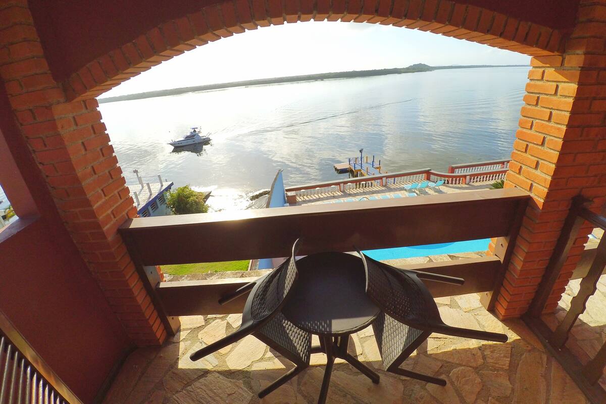 A balcony with a view of a calm lake, a boat, and a distant island.