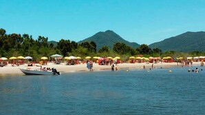 A beach with umbrellas and people, a boat, and mountains in the background. - Hotel Marazul (Cananeia)