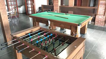 A billiards table and a foosball table in a room with brick walls and a tiled floor.