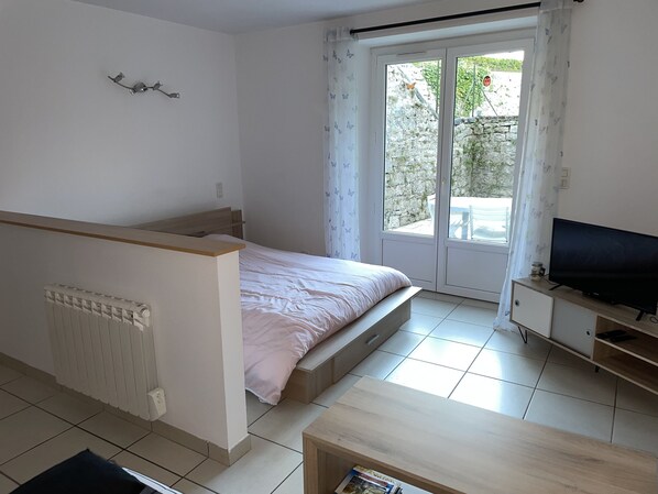Un dormitorio con cama, televisor, radiador y puerta corrediza de vidrio a un balcón.