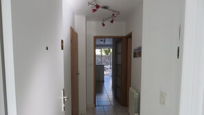 Un pasillo estrecho con suelo de baldosas blancas, puertas de madera y techo con focos rojos.