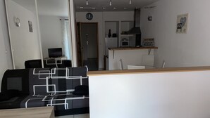 Un espacio habitable compacto con kitchenette, comedor y zona de estar con sofá y mesa.