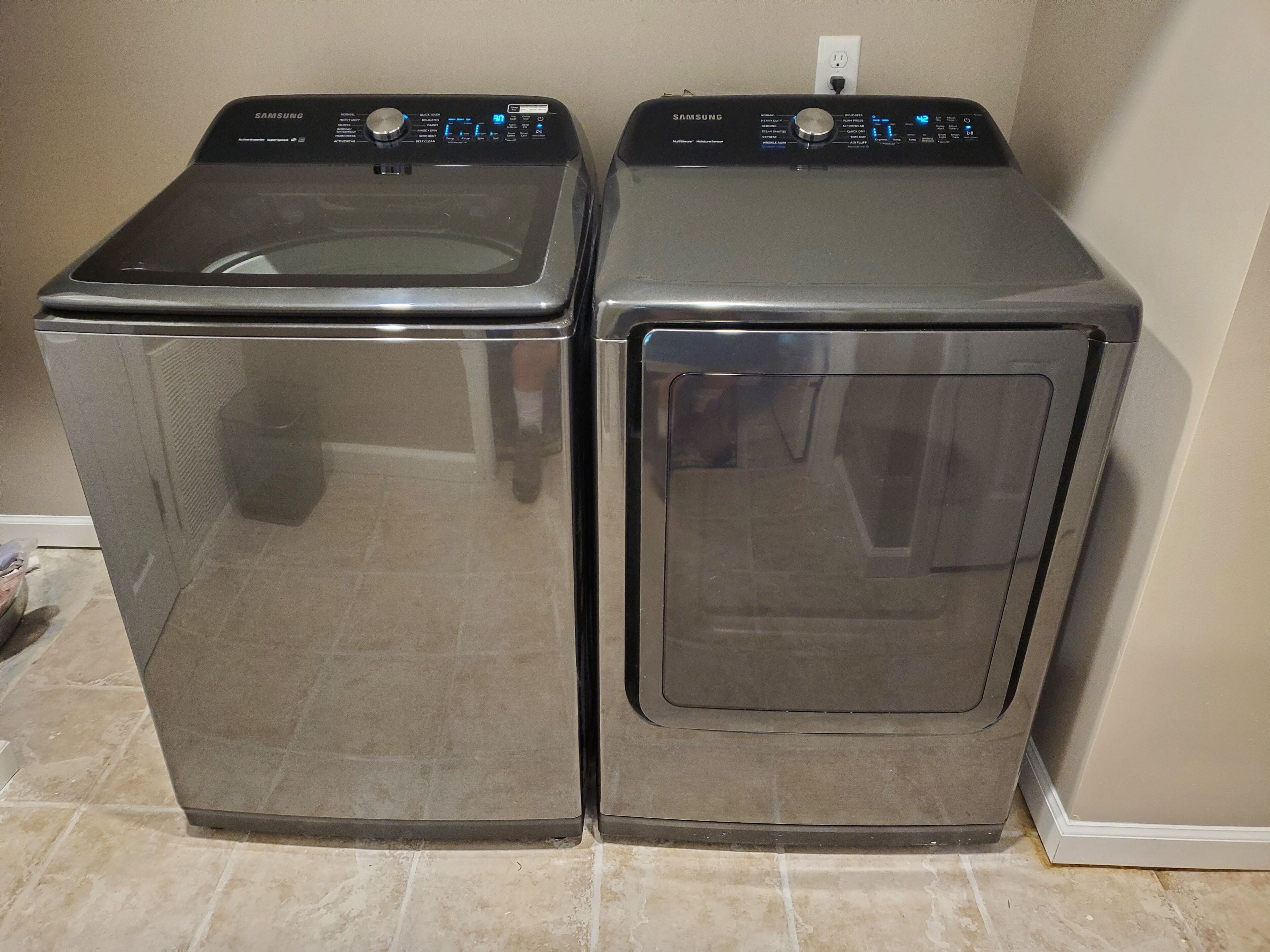 Two front-loading Samsung washing machines in a corner with a tiled floor.
