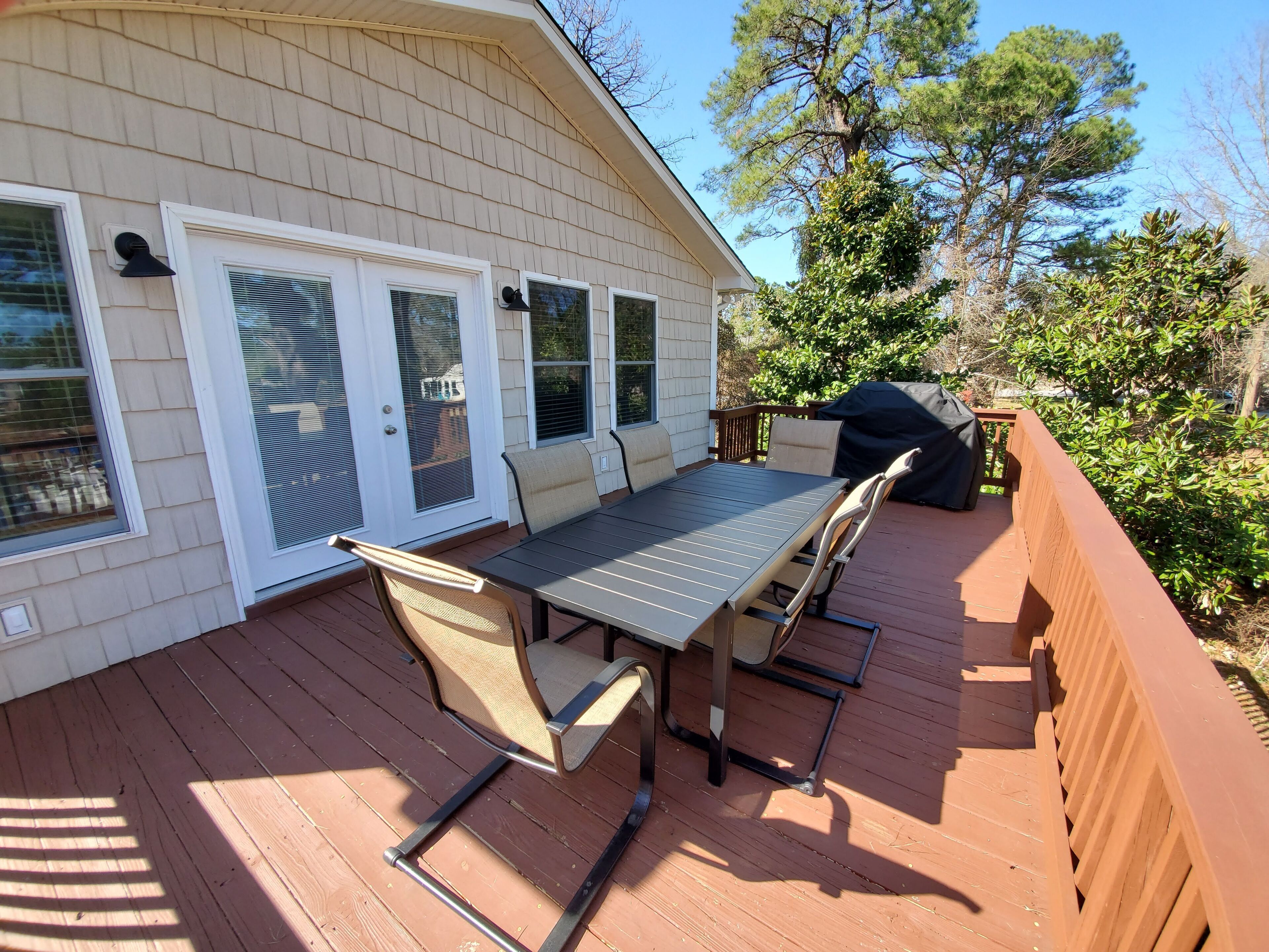 A covered patio with a table and chairs, a grill, and a wooden deck.