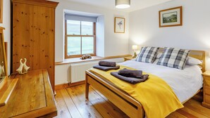 A bedroom with a wooden bed, a window with a view, a radiator, and a wooden wardrobe.