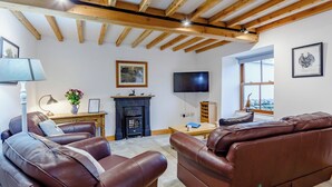 A living room with a fireplace, leather sofas, a TV, and wooden beams on the ceiling.