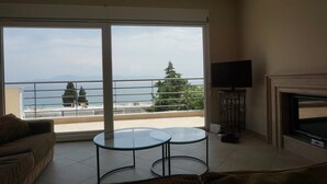 A living room with a sofa, two glass tables, a TV, and a fireplace. - Villa Seaview          . (Palio, Kavala)