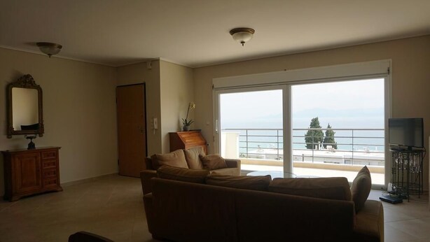 A living room with a sofa, a television, and a view of the sea through large windows. - Villa Seaview          . (Palio, Kavala)