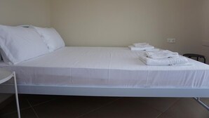 A neatly made bed with white linens and pillows, a small round table with a folded white towel, and a wall socket. - Villa Seaview          . (Palio, Kavala)