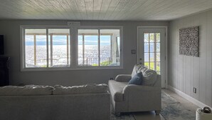 A room with a large window overlooking a coastal view, a sofa, and a decorative wall piece. - Lakefront Paradise - Sleeps 6 - Only $400/Night (Pulaski)