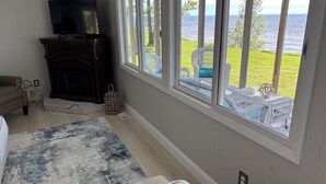 A living room with a fireplace, a television, and a large window overlooking a grassy area and water. - Lakefront Paradise - Sleeps 6 - Only $400/Night (Pulaski)