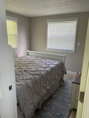 A bedroom with a bed, two windows with blinds, a radiator, and a patterned rug. - Lakefront Paradise  - Sleeps 6 - Only $400/Night  (Pulaski)