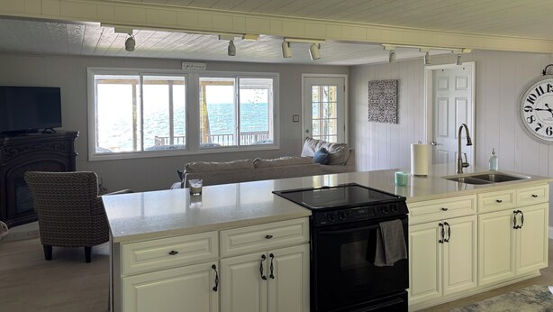 A kitchen with a large island, white cabinetry, a black stove, and a view of the ocean through large windows. - Lakefront Paradise - Sleeps 6 - Only $400/Night (Pulaski)