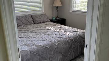 A bedroom with a bed, a nightstand, a lamp, and a window with blinds.