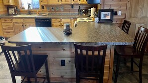 Una cucina con mobili in legno, un piano di lavoro in granito, un piano cottura integrato e una sveglia appesa al muro.
