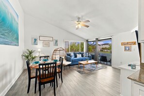A spacious living area with a dining table, blue sofa, and a ceiling fan. - Steps to Beach - Cozy Fall Condo, Sleeps 4 (Destin)