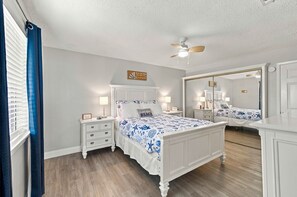 Une chambre à coucher comprenant un lit, des tables de chevet, une commode, un ventilateur de plafond et un grand miroir.