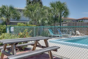 A fenced pool area with a picnic table, lounge chairs, and palm trees.