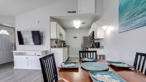 A modern kitchen with white cabinetry, a flat-screen TV mounted above the counter, and a dining area with a wooden table set for four. - Cozy Condo, 3 Minute Walking Distance to the Beach (Destin)