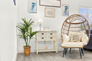 A room with a wicker chair, a potted plant, a small white side table with drawers, and wall art. - Steps to Beach - Cozy Fall Condo, Sleeps 4 (Destin)