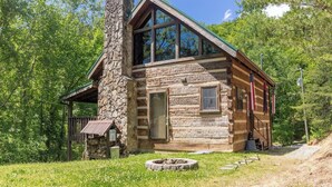 Eine rustikale Holzhütte mit einem Steinkamin, großen Fenstern und einer kleinen Veranda.
