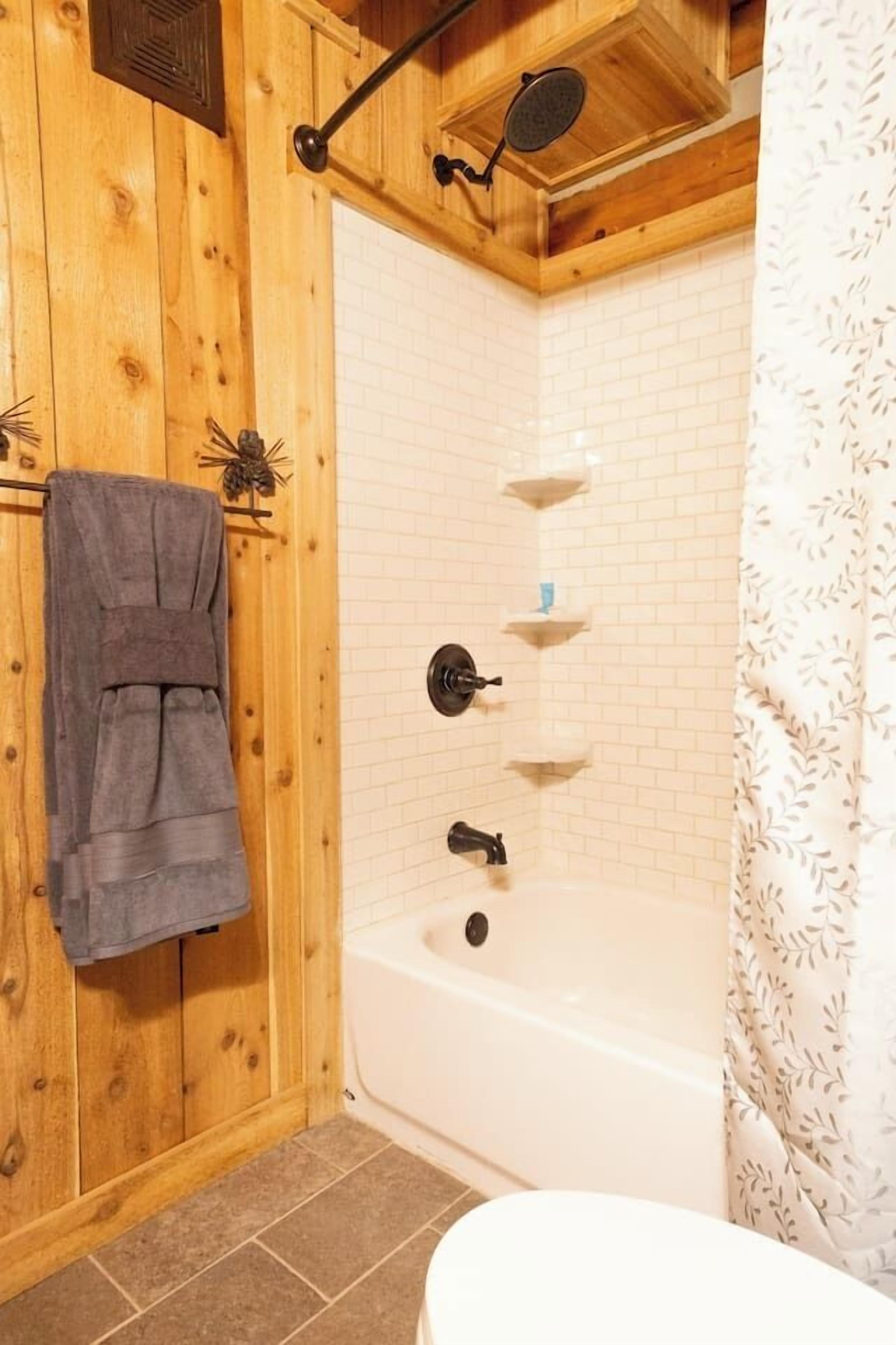 Ett badrum med träpanel, badkar, handduksställ och duschdraperi.