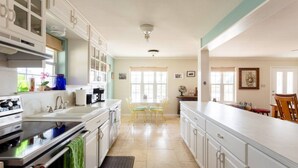 A kitchen with white cabinets, a stove, a sink, and a dining area with chairs and a table.