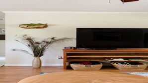 A living room with a flat-screen TV on a wooden stand, a vase with dried plants, and two wicker baskets under the stand.