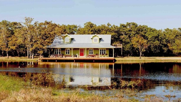 A house with a dock extending into a lake, surrounded by trees.