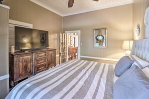 A bedroom with a large bed, a wooden dresser, a television, and a mirror. - Country-Chic Cotter Home w/ Outdoor Living Space! (Cotter)