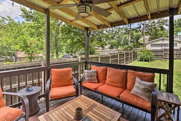 A covered outdoor patio with a wooden deck, orange cushioned seating, and a table with a vase. - Country-Chic Cotter Home w/ Outdoor Living Space! (Cotter)