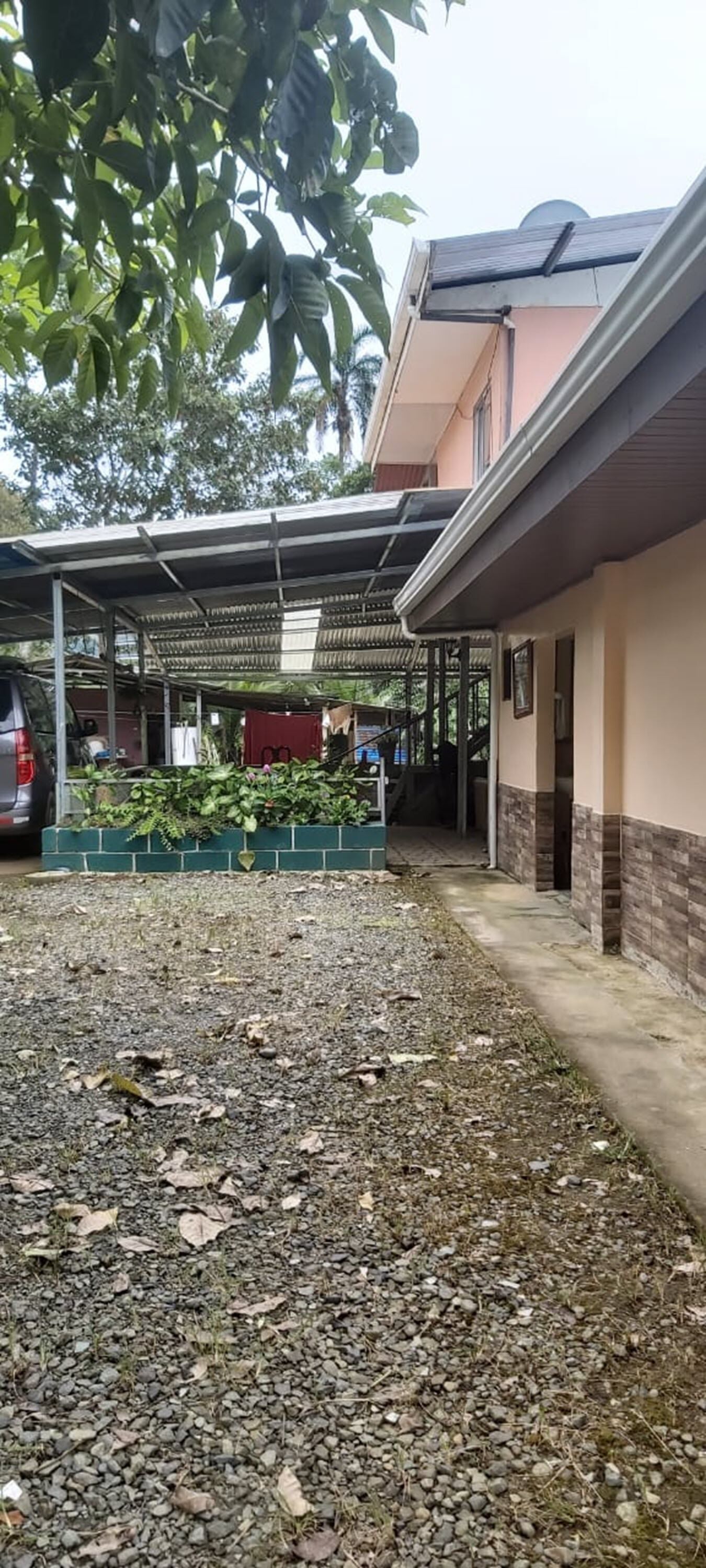 Un espacio exterior cubierto con suelo de grava, un coche aparcado y un edificio con fachada color beige y un porche cubierto.