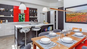 Eine moderne Küche mit Essbereich, mit einem großen Gemälde, einem Holzesstisch für sechs Personen und einer Bar mit Hockern.