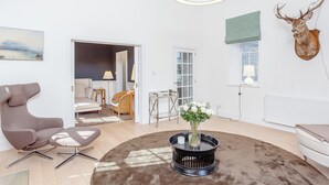 Ein modernes Wohnzimmer mit einem runden Couchtisch, einem braunen Teppich, einem aufgehängten Hirschgeweih und einem Bild an der Wand.