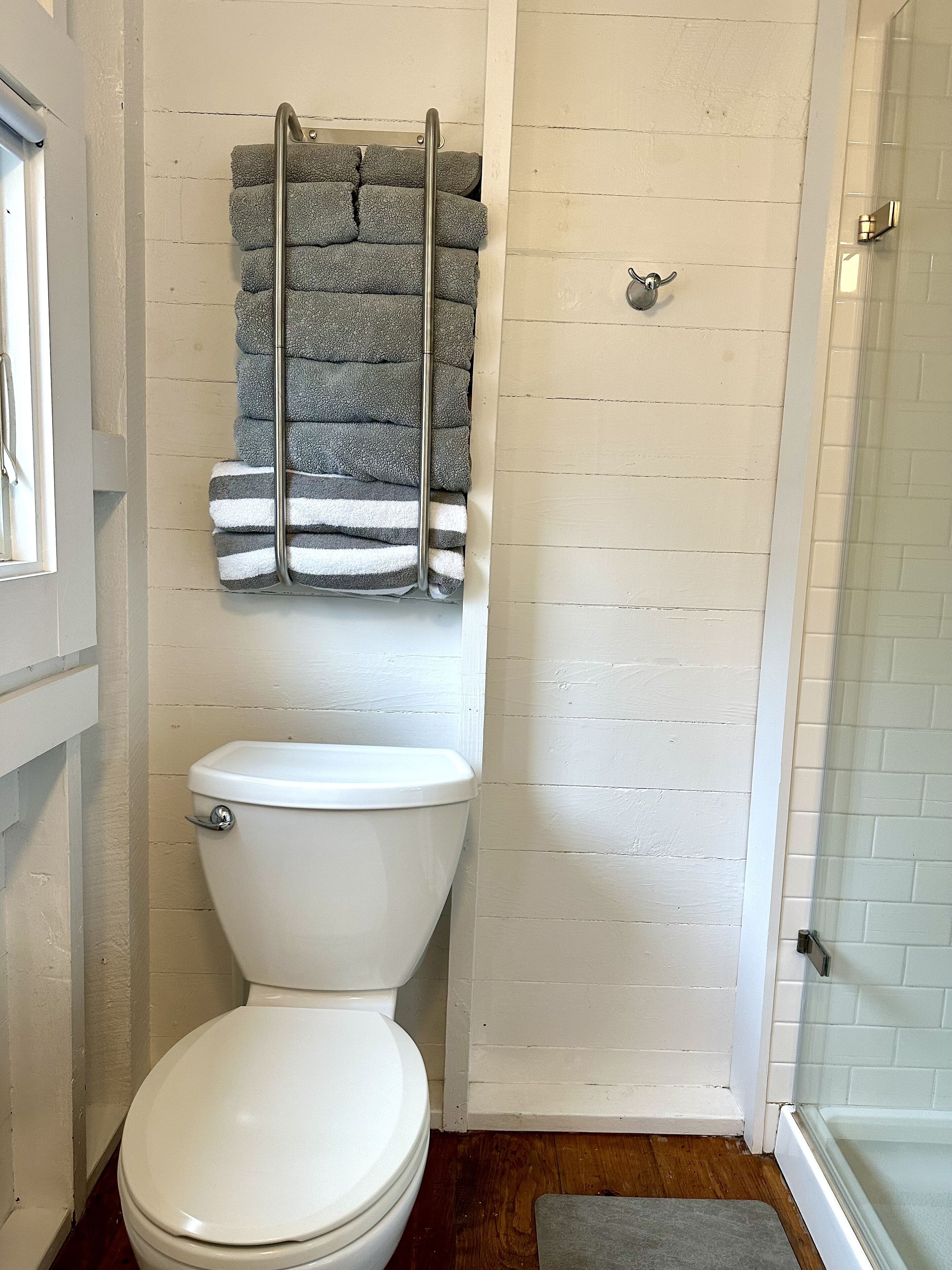 Un baño con un inodoro blanco, un perchero con toallas dobladas y una zona de ducha.