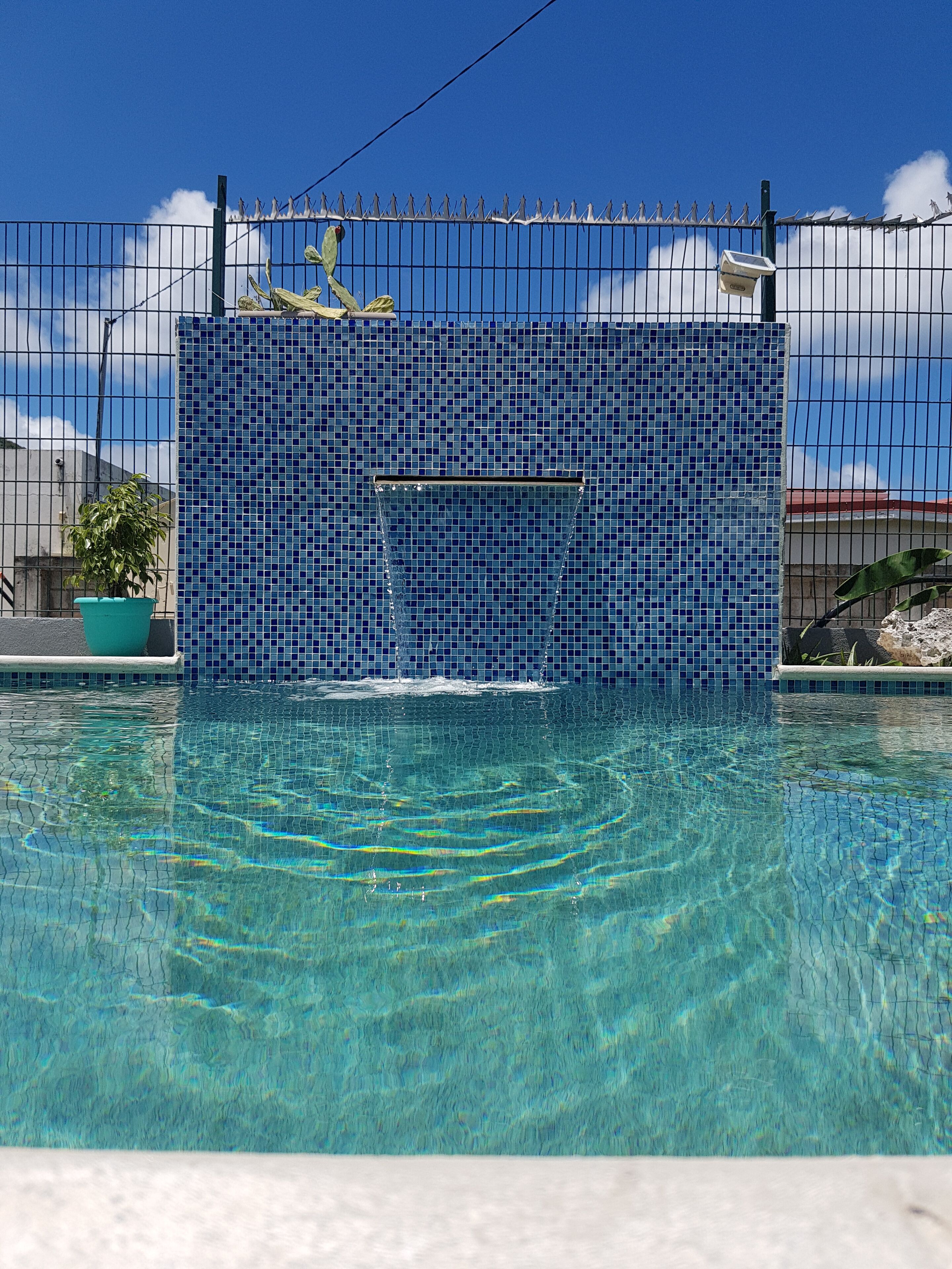 A clear pool with a tiled wall and a metal fence.