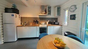 A compact kitchen with white cabinets, a stove, and a sink. There is a wooden table with a fruit bowl in the center. - Stunning terraced Logcabin House with pool  (Saint Martin)